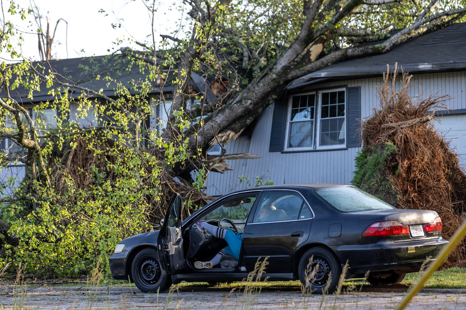 Carolyn Gillman has to stay in her car now on Briarwood Circle in Rockdale County with her cat Boi after a tree smashed through her house. Cleanup efforts were underway Wednesday, April 3, 2024. The National Weather Service confirmed a tornado over Conyers around 11:54 p.m. Tuesday. (John Spink / John.Spink@ajc.com)