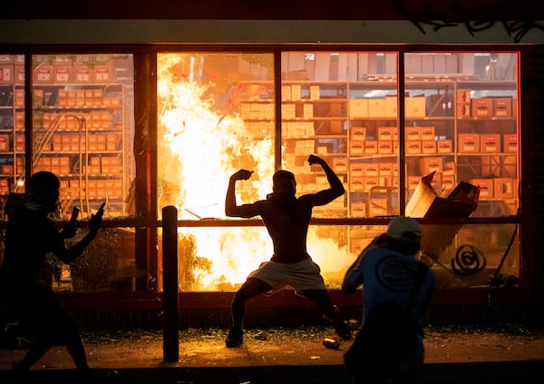 A man poses  in front of a fire at an AutoZone store, while protesters hold a rally for George Floyd in Minneapolis on Wednesday night. 