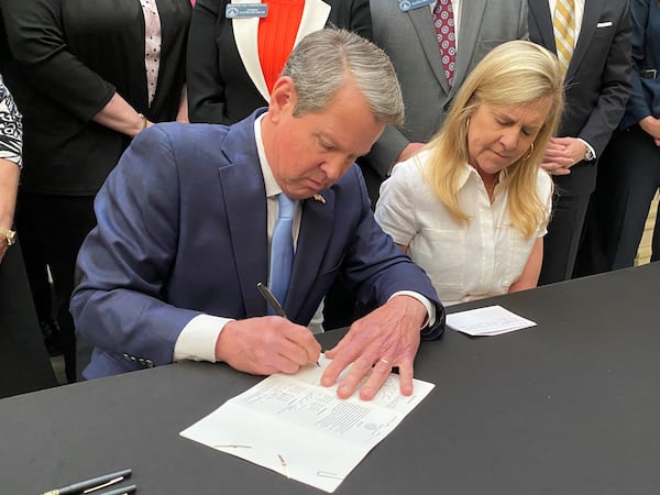 Gov. Brian Kemp signs SB 65, a bill to establish a state-based exchange under the Affordable Care Act, where Georgians could shop for ACA health insurance plans on a state-run website. Kemp is flanked by his wife, Marty, and sits before a crowd of legislators at the Georgia Capitol on Tuesday, May 2, 2023. (PHOTO by Ariel Hart)