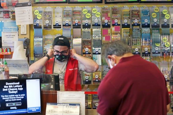 A clerk adjusts his protective mask while waiting on a masked customer at Ted’s Stateline Mobil in Massachusetts. Many states that don’t offer online lottery options have struggled during the pandemic.