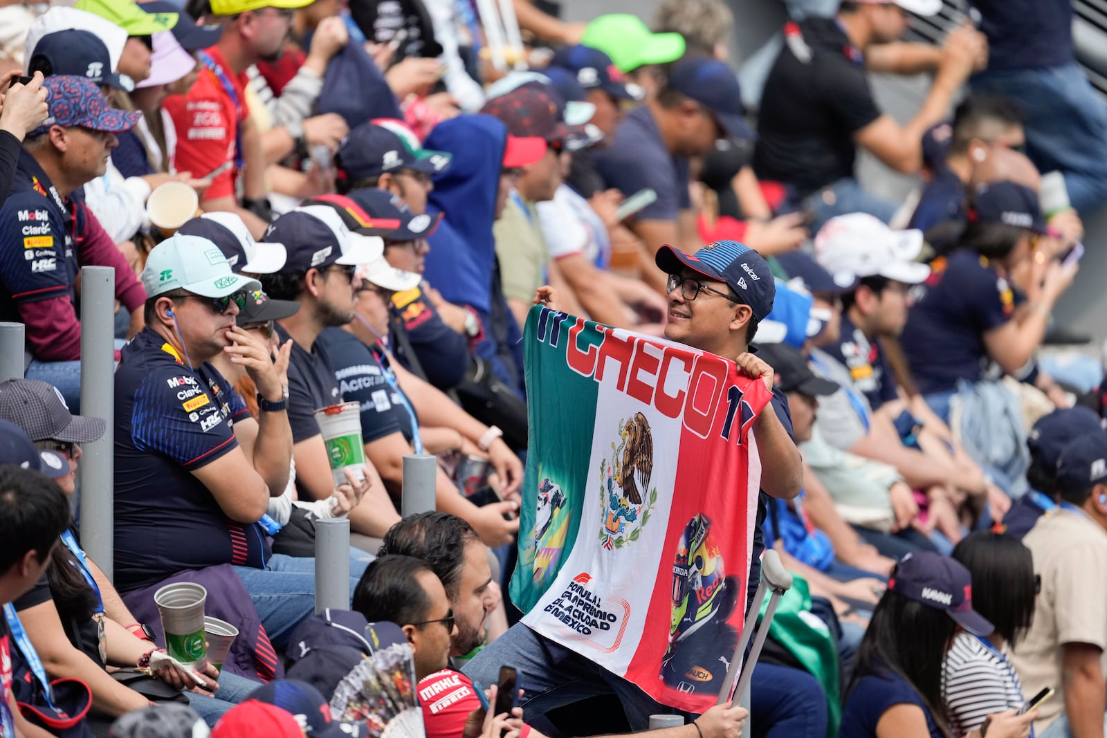 A fan of Red Bull driver Sergio Perez poses for photos with a Mexican flag during the third free practice ahead of the Formula One Mexico Grand Prix auto race at the Hermanos Rodriguez racetrack in Mexico City, Saturday, Oct. 26, 2024. (AP Photo/Eduardo Verdugo)