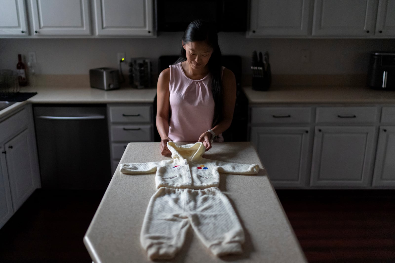 Leah Elmquist stands with the outfit she traveled in when she was adopted from Korea at five months old to a family in America, Monday, June 24, 2024, at her home in Las Vegas. (AP Photo/David Goldman)