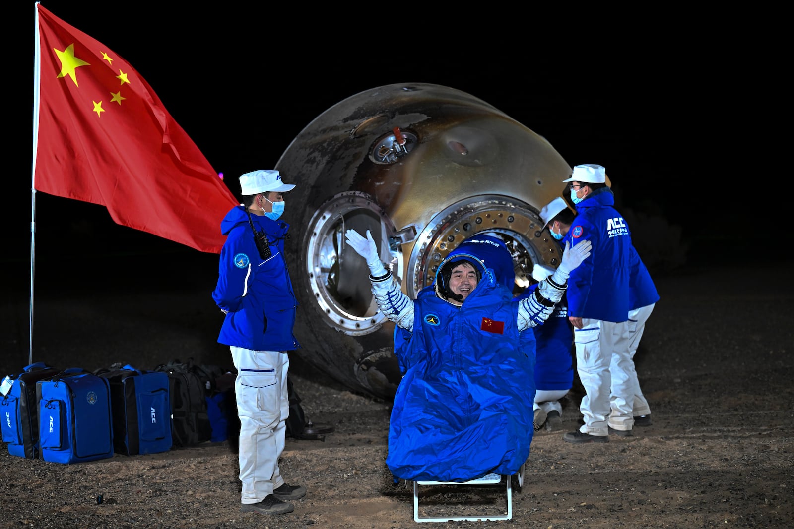 In this photo released by Xinhua News Agency, astronaut Ye Guangfu waves near the re-entry capsule of the Shenzhou-18 manned space mission after it landed successfully at the Dongfeng landing site in northern China's Inner Mongolia Autonomous Region in the early Monday, Nov. 4, 2024. (Li Xin/Xinhua via AP)