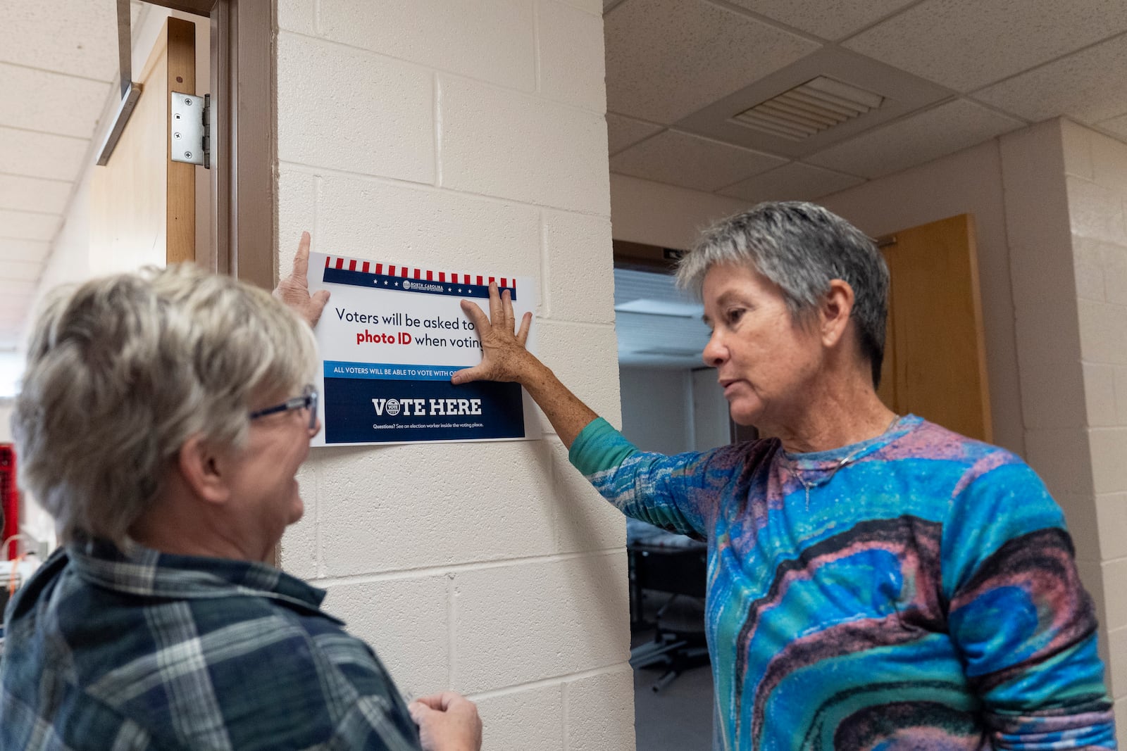 Poll workers hang signs at an early in-person voting site at Asheville-Buncombe Technical Community College, on Oct. 16, 2024, in Marshall, N.C. (AP Photo/Stephanie Scarbrough)