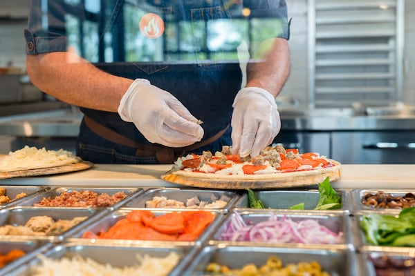 Wearing food-safe gloves, an employee at Blaze Pizza assembles ingredients for a custom pie. (Courtesy of Blaze Pizza)