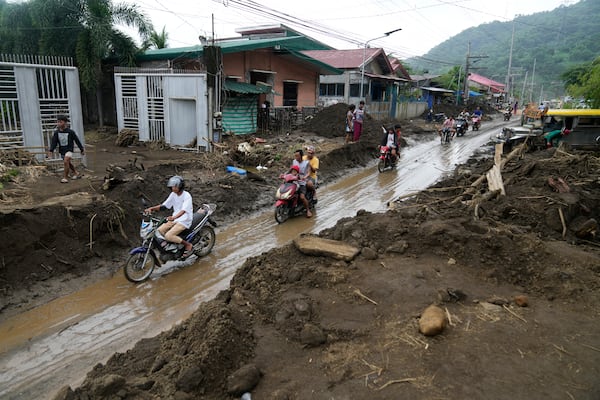 Residents ride motorcycles along a mud covered road after a landslide triggered by Tropical Storm Trami, recently struck Talisay, Batangas province, Philippines, Saturday, Oct. 26, 2024 . (AP Photo/Aaron Favila)