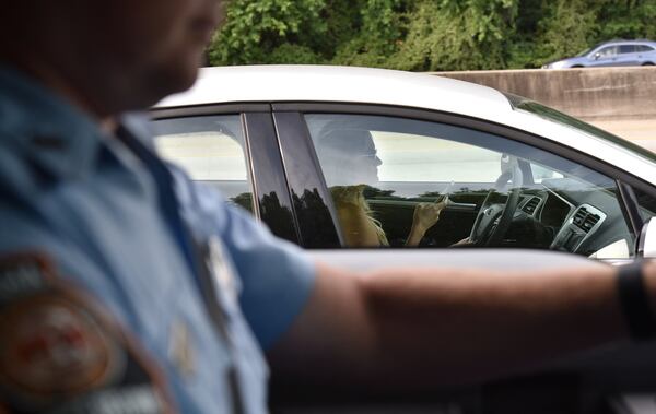 A driver apparently uses a phone while driving as Sgt. First Class Chris Stallings monitors motorists in downtown Atlanta on Thursday. In one week, police officers across the state will begin enforcing the Hands-Free Georgia Act, which prohibits motorists from holding their phones or other electronic devices while driving. HYOSUB SHIN / HSHIN@AJC.COM