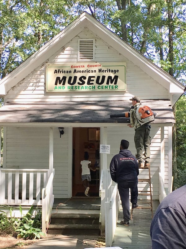 Clifton Fisher III, president of the African-American Alliance (administrative board for the Coweta County African-American Museum), holds the ladder for volunteer Paul Manns as he blows leaves from the museum’s roof. Both Manns and Fisher are members of South Atlanta Progress, which initially formed to improve race relations. CONTRIBUTED