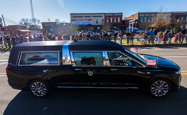 The hearse for former President Jimmy Carter passes through Plains, Georgia, in a motorcade on Saturday, Jan. 4, 2025, following his death earlier this week. The procession will then head to Atlanta where Carter will lie repose at the Carter Center. (Arvin Temkar/The Atlanta Journal-Constitution/TNS)