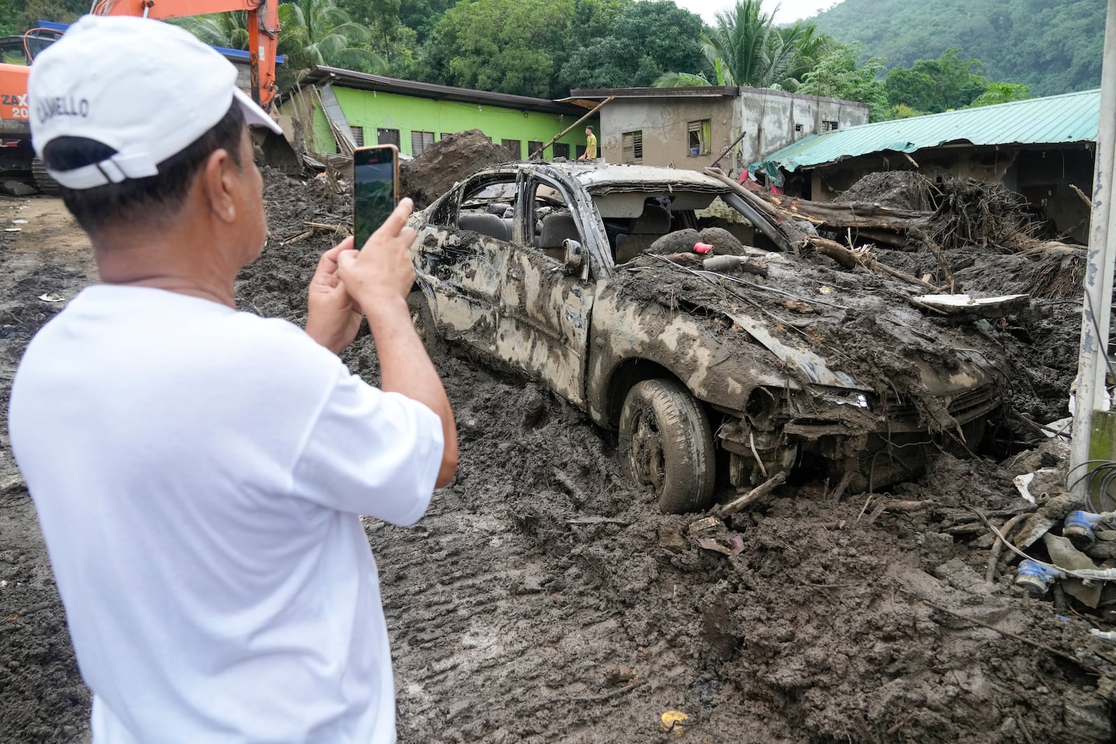 A villager takes a photo of a damaged car after a recent landslide triggered by Tropical Storm Trami struck Talisay, Batangas province, Philippines leaving thousands homeless and several villagers dead on Saturday, Oct. 26, 2024. (AP Photo/Aaron Favila)