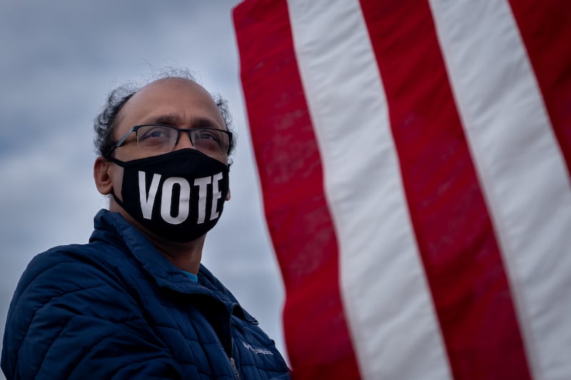 Vijay Vemulapalli, a volunteer with South Asian mobilizing group They See Blue, waves an American flag at a rally in the metro-Atlanta area in support of Democratic Senate candidates Jon Ossoff and Rev. Raphael Warnock on Dec. 20, 2020. (Arvin Temkar / AJC)