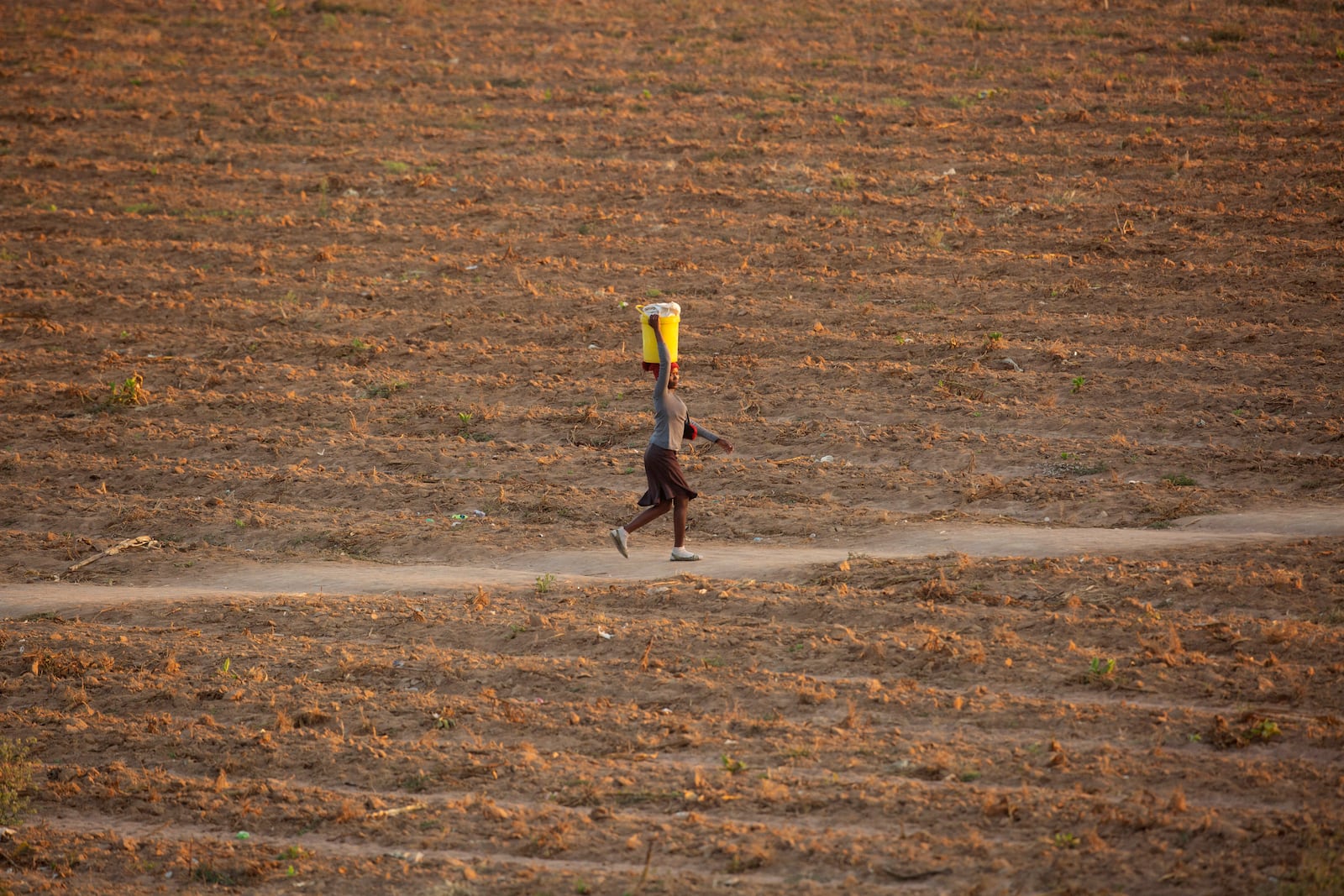 FILE - A woman walks along a path in a drought-stricken field in Zvimba, rural Zimbabwe, Saturday, June, 26, 2021. (AP Photo/Tsvangirayi Mukwazhi, File)