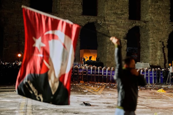 A man holds a Turkish flag with the image of Turkey's founding father Mustafa Kemal Ataturk in front of anti riot police officers during a protest against the arrest of Istanbul's Mayor Ekrem Imamoglu in Istanbul, Turkey, Friday, March 21, 2025. (AP Photo/Emrah Gurel)