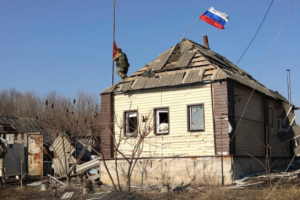 In this photo taken from video distributed by Russian Defense Ministry Press Service on Friday, March 14, 2025, a Russian soldier rises a red flag atop of a house at an area in the Kursk region of Russia after it was taken over by Russian troops. (Russian Defense Ministry Press Service via AP)