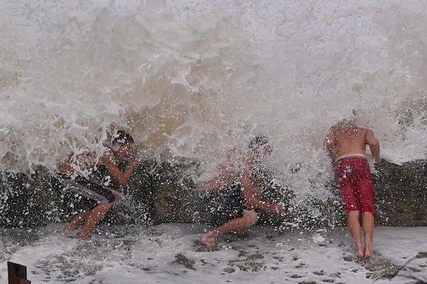 Children take shelter from waves behind a breakwall in the Coolangatta area of Gold Coast, Australia, Friday, March 7, 2025. (Dave Hunt/AAP Image via AP)