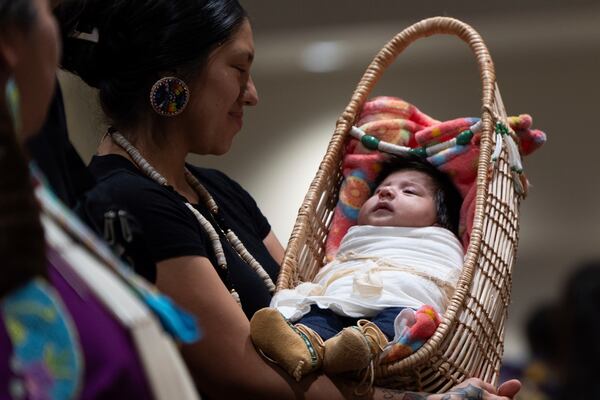 Kimberly Jurado holds her daughter, Delia Rubi Jurado, as they walk during a dance at a powwow at Chinook Winds Casino Resort, Saturday, Nov. 16, 2024, in Lincoln City, Ore. (AP Photo/Jenny Kane)