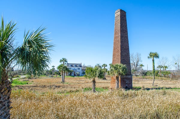 One mile south of Darien on U.S. Highway 17 sits Butler Island, the former site of a large rice plantation. A tall brick chimney, the remains of a steam-powered rice mill, is one of two surviving structures from the original plantation. Over a two-day period in 1859, 436 people enslaved at Butler Island Plantation were sold at auction in Savannah, an event referred to as the Weeping Time. The white house on the current property was built in the mid-1920s by former owner Col. T.L. Huston. Today the Georgia Department of Natural Resources manages the grounds. The Huston House, which is not inhabited nor maintained, was placed on the Georgia Trust for Historic Preservation’s “Places in Peril” list in 2019. COURTESY OF THE COLLECTIVE & CO