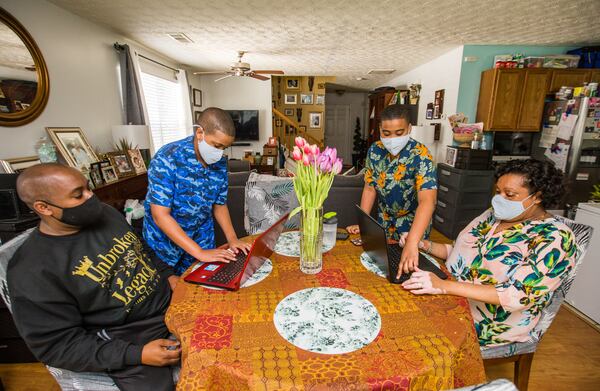 Earl McCarthy, left, and his wife Natasha Pierre McCarthy, seated right, get help from their children Joshua, 12, left, and Aidan, 14, right, setting up laptops Monday, April 5, 2021.  Their oldest daughter is away at college. Earl lost his job in sales at the beginning of the pandemic and Natasha, an adjunct professor, had to choose between going back to in-person teaching or staying with her kids who are still schooling from home without the option to go back.  (Jenni Girtman for The Atlanta Journal-Constitution)