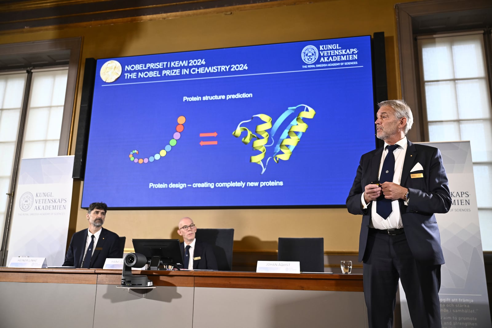 Johan Åqvist, right, member of the Nobel Committee for Chemistry, explains the work of David Baker, Demis Hassabis, and John M Jumper, winners of this years Nobel Prize in Chemistry at the Royal Swedish Academy of Sciences, in Stockholm, Sweden, Wednesday, Oct. 9, 2024. (Christine Olsson/TT News Agency via AP)