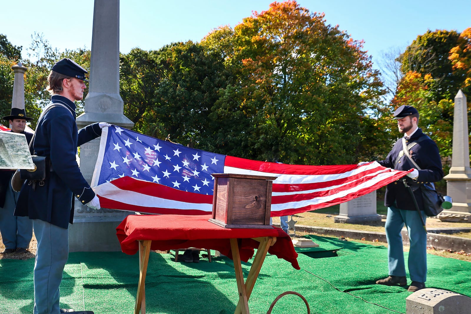 In this photo provided by The Valley Breeze, Civil War re-enactors fold an American flag near an urn, center, containing the cremated remains of Byron R. Johnson, a Union soldier who was born in Pawtucket, R.I., in 1844 and fought in the Civil War, during funeral services, Wednesday, Oct. 16, 2024, at Oak Grove Cemetery, in Pawtucket, after his remains were transferred from storage at a cemetery in Seattle. (Charles Lawrence/The Valley Breeze via AP)