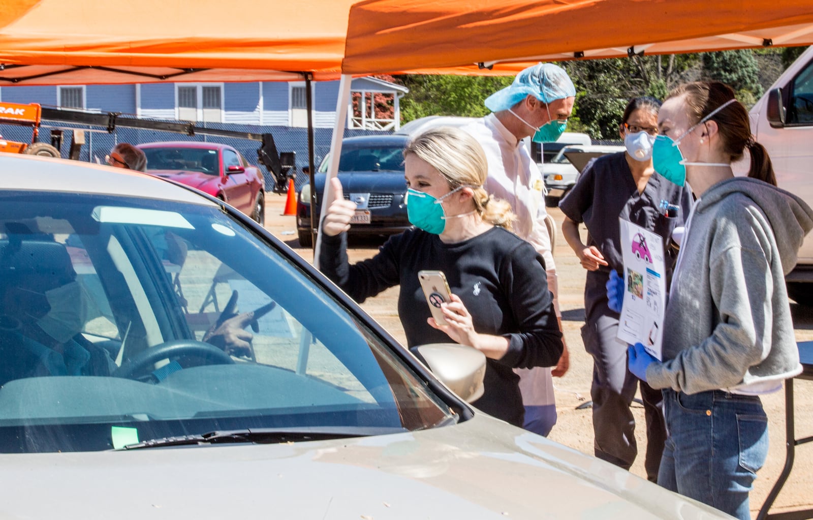 Rebekah Kemp, a practice administrator for Ethne Health (left), and Lauren Purser (right), who normally is a flight attendant, try to communicate through closed windows while registering motorists showing symptoms of COVID-19 on Friday, April 3, 2020. Ethne Health — in partnership with the city of Clarkston, community churches and food banks — is providing free coronavirus testing and food for people showing symptoms who live in the Clarkston area. The testing will continue on Saturday. (Jenni Girtman for the Atlanta Journal-Constitution)