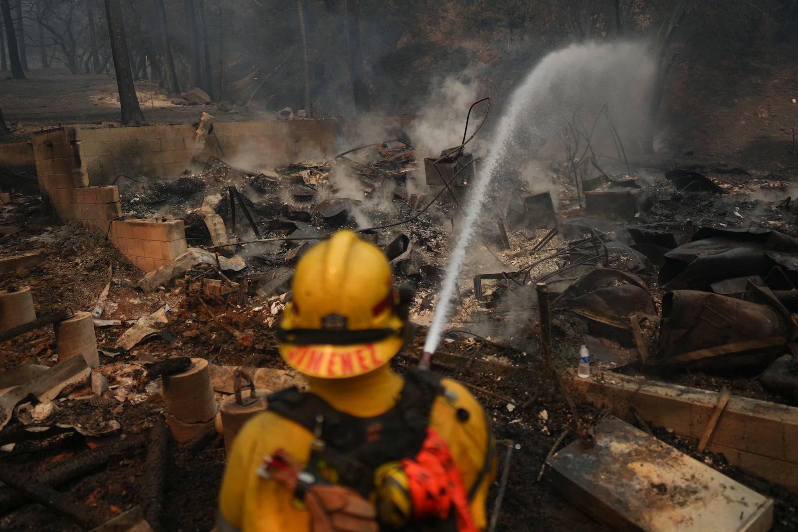 A firefighter hoses down hot spots on a fire-ravaged property while battling the Bridge Fire Wednesday, Sept. 11, 2024, in Wrightwood, Calif. (AP Photo/Eric Thayer)