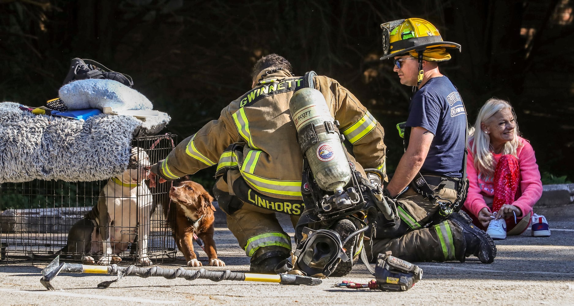 Gwinnett County firefighters, Wesley Linhorst (left) and Chase Schreckengost (center) pet the dogs that fire victim Pauline Bush (right) was watching when she was startled from sleep Thursday morning by firefighters who were banging at her door. (John Spink / John.Spink@ajc.com)

