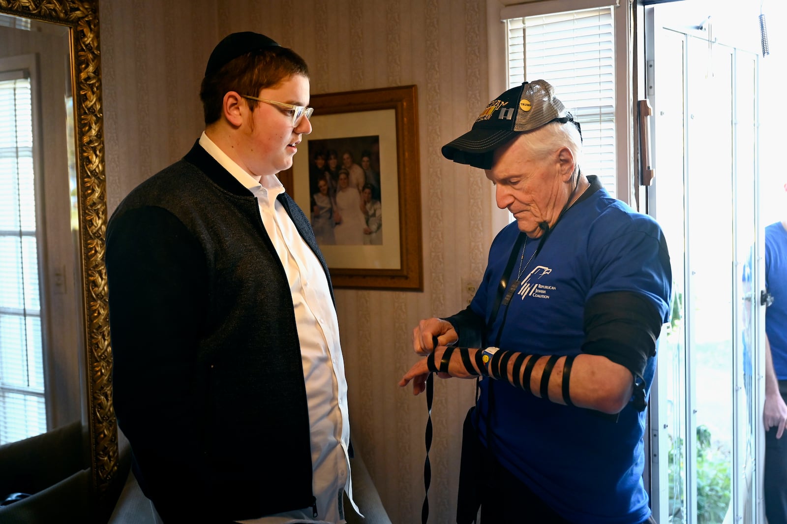 Republican Jewish Coalition member David Cuttner, right, begins to place Tefillin, a set of small black leather boxes with leather straps containing scrolls of parchment inscribed with verses from the Torah, on himself in the home of Menachem Kogan, Sunday, Oct. 27, 2024, in West Bloomfield Township, Mich. (AP Photo/Jose Juarez)