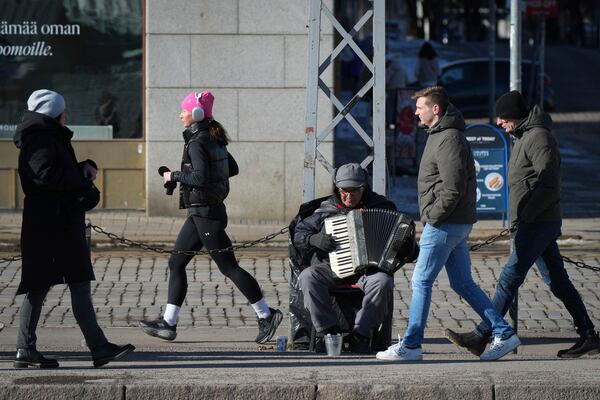 People walk past a street musician in the center of Helsinki, Finland, Saturday, March 15, 2025. (AP Photo/Sergei Grits)