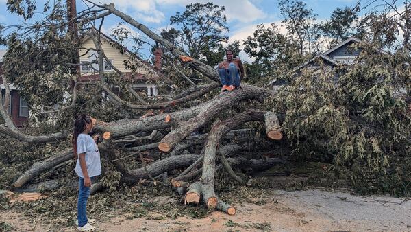 Qena Fabin, an Augusta resident, sits on top of an oak tree that toppled into her front yard because of Tropical Storm Helene while her 7-year-old daughter looks on. Fabin has to walk around the tree's massive roots or scramble over it to leave her yard. (Mirtha Donastorg/The Atlanta Journal-Constitution/TNS)