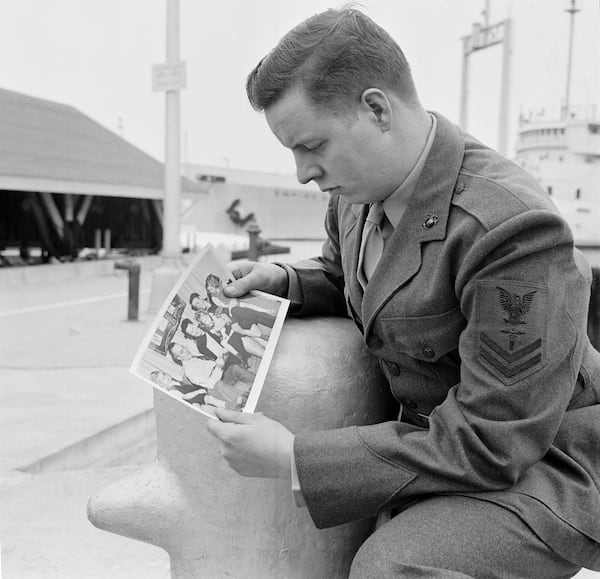 FILE - United States Navy Pharmacist's mate Donald Martin looks at a 1952 Christmas photo of his missing family at Fort Schuyler in New York, April 2, 1959. (AP Photo, File)