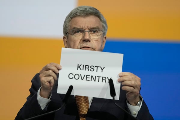 IOC President Thomas Bach holds up the name of Kirsty Coventry as she is announced as the new IOC President at the International Olympic Committee 144th session in Costa Navarino, western Greece, Thursday, March 20, 2025. (AP Photo/Thanassis Stavrakis)