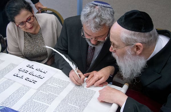 Aviva Postelnik (left) sits next to her husband, Eyal Postelnik, as Moshe Klein shows Postelnik were to finish the last passage to the historic Torah scroll at Chabad of Cobb on Sunday, March 8, 2020. (Photo: STEVE SCHAEFER / SPECIAL TO THE AJC)