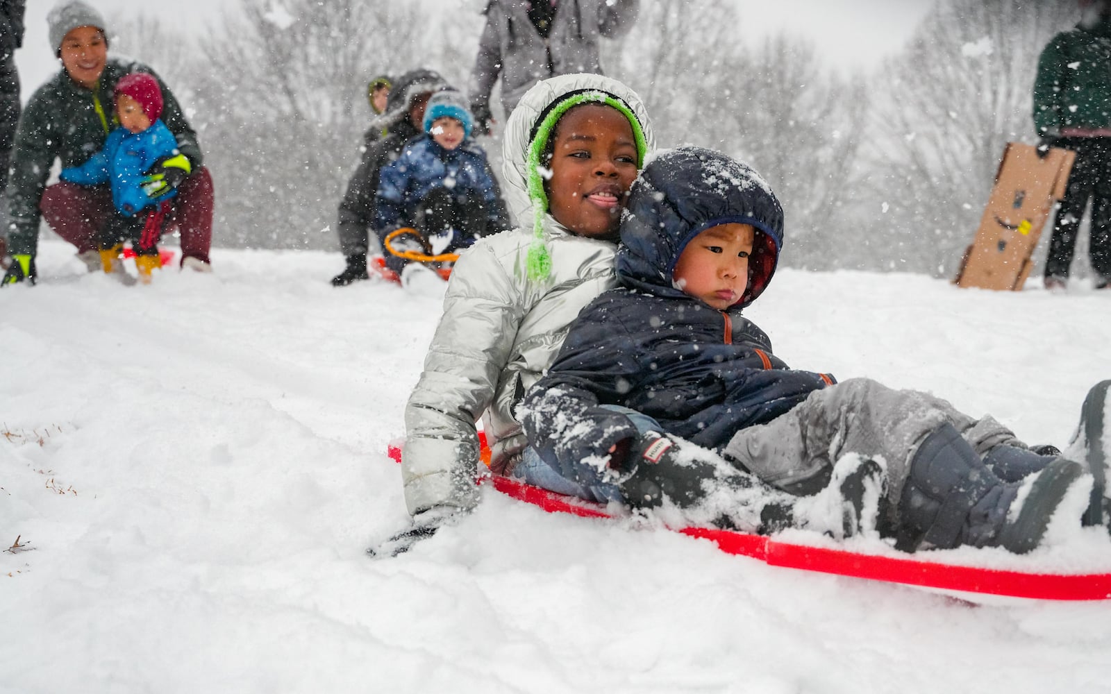 Four year old Weusi Carroll (back) and four year old Parker Cheng ride down a hill on a sled in Piedmont Park. Friday, January 10, 2025 (Ben Hendren for the Atlanta Journal-Constitution)