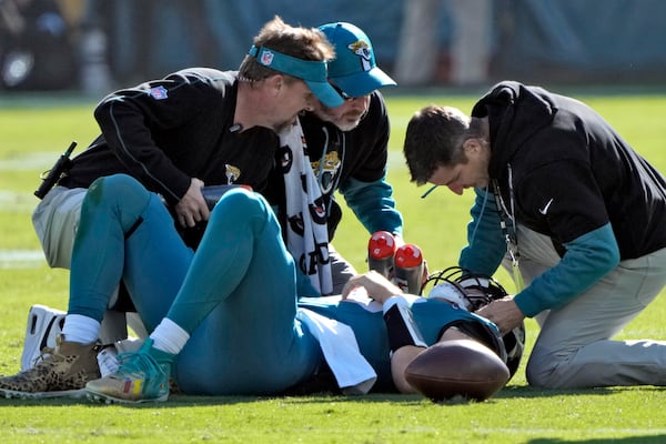 Jacksonville Jaguars quarterback Trevor Lawrence (16) is looked at by trainers after a late hit by Houston Texans linebacker Azeez Al-Shaair (0) during the first half of an NFL football game Sunday, Dec. 1, 2024, in Jacksonville, Fla. (AP Photo/John Raoux)