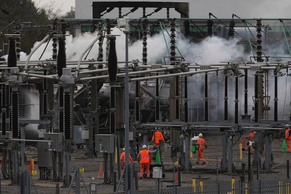 Workers are seen as smoke rises from the North Hyde electrical substation, which caught fire last night, leading to the closure of the Heathrow Airport, in London, Friday March 21, 2025.(AP Photo/Kirsty Wigglesworth)