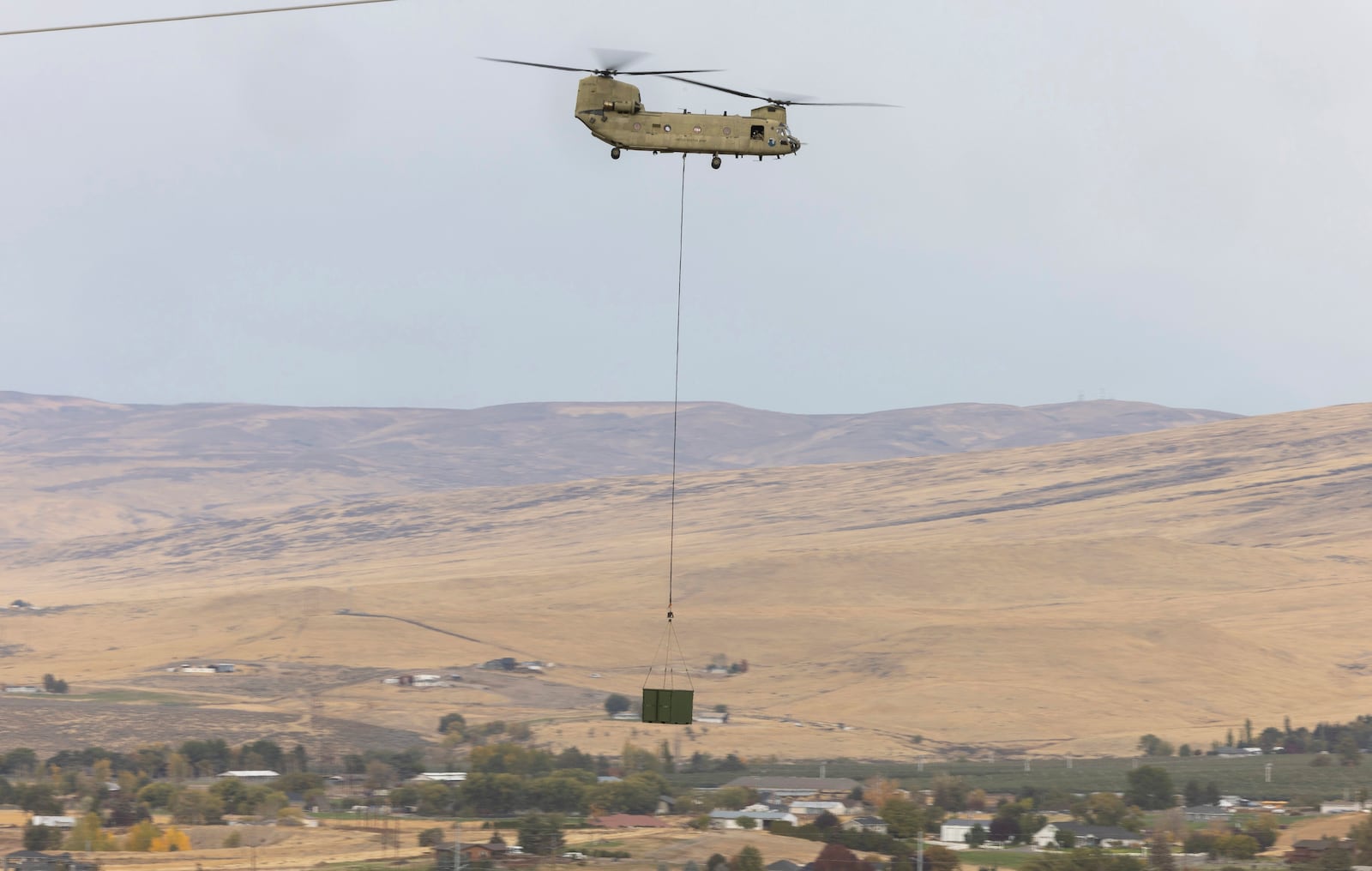 A U.S. Army Chinook helicopter lifts a cargo box out of Vagabond Army Heliport as it heads toward the site of the crashed Navy EA-18G Growler jet on Friday, Oct. 18, 2024, in Yakima, Wash. (Nick Wagner/The Seattle Times via AP)