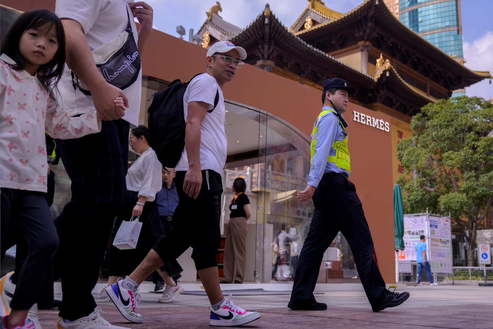 People tour as a promoter waits for customers at a luxury fashion boutique booth set up near the Jing'an Temple at a popular shopping district in Shanghai, China, Saturday, Oct. 12, 2024. (AP Photo/Andy Wong)