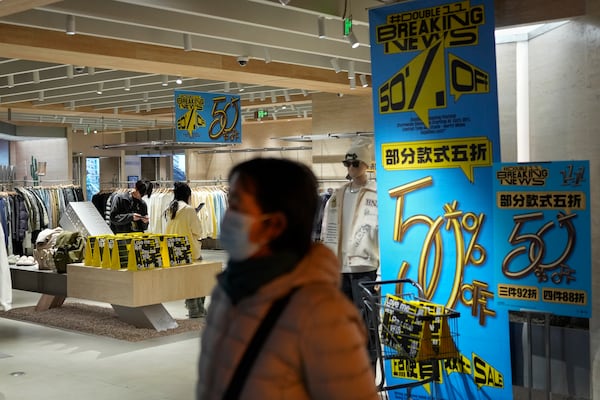 A masked woman walks at a fashion boutique displaying posters to promote Singles' Day discounts at a shopping mall in Beijing, Monday, Nov. 11, 2024. (AP Photo/Andy Wong)