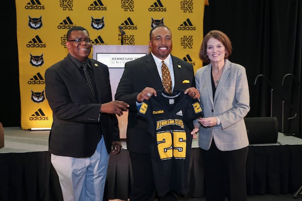 Kennesaw State coach Jerry Mack, center, holds a KSU jersey next to Director of Athletics Milton Overton, left, and President Kathy S. Schwaig during his introductory event as the new football coach at the KSU Convocation Center, Tuesday, December 3, 2024, in Kennesaw, Ga. Mack replaces Kennesaw State coach Brian Bohannon, who was has been the program’s only coach since its inception in 2015. Jason Getz / AJC)
