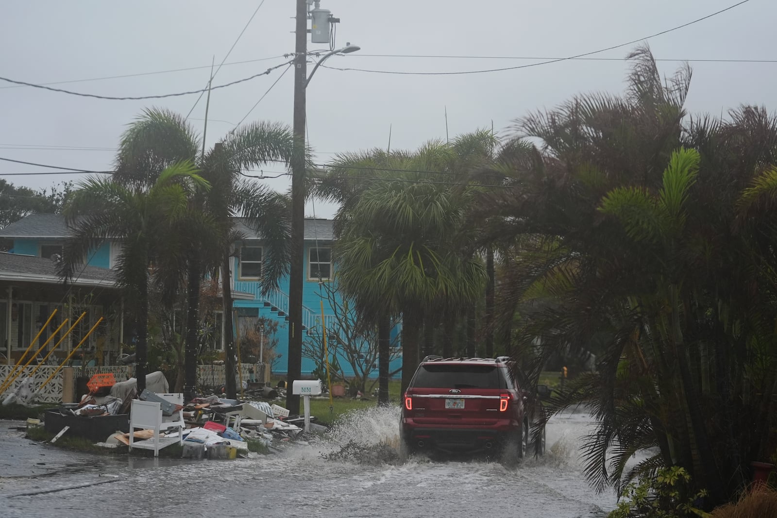 A car drives past a pile of debris from Hurricane Helene flooding, along a street that had already begun flooding from rain ahead of the arrival of Hurricane Milton, in Gulfport, Fla., Wednesday, Oct. 9, 2024. (AP Photo/Rebecca Blackwell)