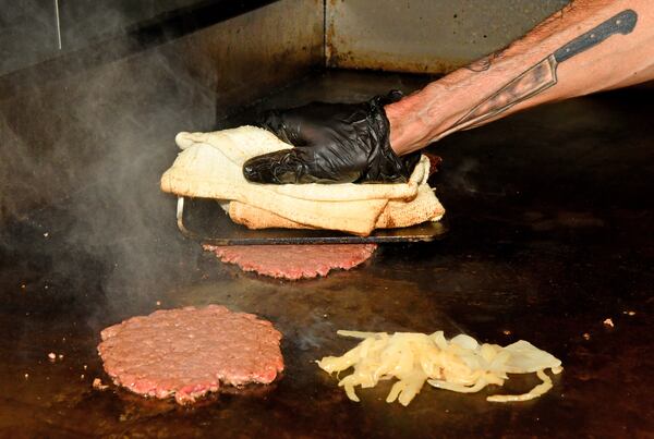 Chef Brian Hill does what makes a smash burger a smash burger with a heavy hot iron implement on the grill of Local Republic in Lawrenceville. (Chris Hunt for the AJC)