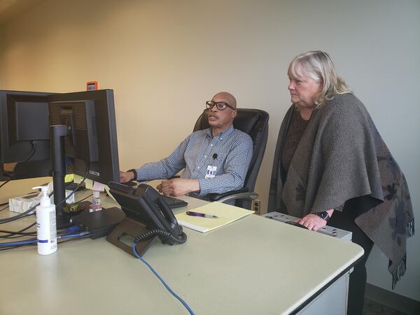 On May 4, 2023, Jody White (left) and Grace Burke of Morton Comprehensive Health Services in Tulsa, Oklahoma, examined a list of the health center’s patients whose Medicaid eligibility was up for review that month. White had spent the morning calling patients on the list to make sure they were aware of the process and offer his assistance. (Bram Sable-Smith/KFF Health News)