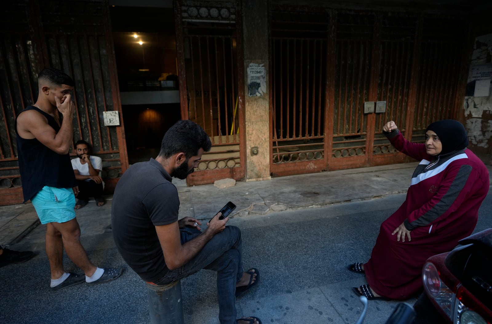 Joumana Hanafi, right, a Lebanese Palestinian woman who fled the ongoing Hezbollah-Israel war in south Lebanon, gathers with displaced men at the entrance of one of Beirut's oldest and best known movie theatres, Le Colisee, where they are sheltering in Beirut, Lebanon, Tuesday, Oct. 22, 2024. (AP Photo/Hussein Malla)