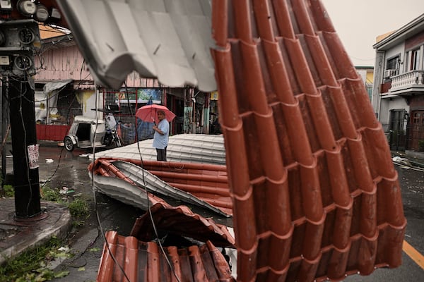 A man walks past roof sheets suspended on electric wires blown by strong winds caused by Typhoon Man-yi along a street in the municipality of Baler, Aurora province, northeastern Philippines, Monday, Nov. 18, 2024. (AP Photo/Noel Celis)