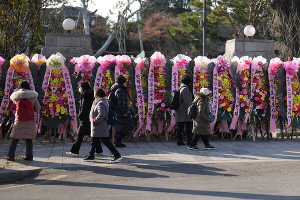 People walk past wreaths sent by supporters of impeached South Korean President Yoon Suk Yeol outside of the Constitutional Court in Seoul, South Korea, Tuesday, Dec. 17, 2024. (AP Photo/Lee Jin-man)