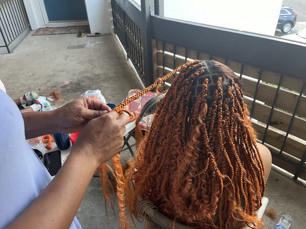 A Honduran renter in Austell braids another woman's hair outside her apartment on Wednesday, August 21, 2024.