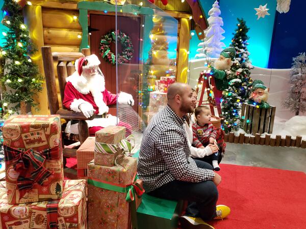 Irina and Adrian Patru brought their 11-month-old baby, Samson, to visit Santa at the Bass Pro Shops store in Duluth. A clear plastic barrier separated families from Santa as a protection during the pandemic. MATT KEMPNER / AJC