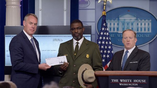 Interior Secretary Ryan Zinke, left, and Harpers Ferry National Historic Park Superintendent Tyrone Brandyburg, accompanied by White House press secretary Sean Spicer, hold up a check during the daily briefing at the White House in Washington, Monday, April 3, 2017. President Donald Trump gave his first quarter salary to the National Park Service. (AP Photo/Susan Walsh)