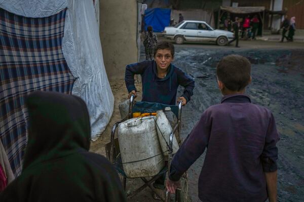 A Palestinian boy pushes a wheelchair carrying jerrycans and plastic bottles with water at a camp for displaced people in Deir al-Balah, Gaza Strip, Thursday, Dec. 12, 2024. (AP Photo/Abdel Kareem Hana)